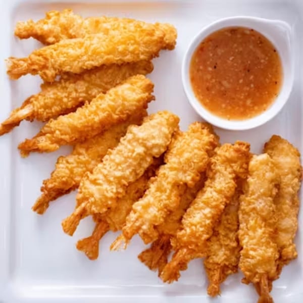 Crispy golden fried shrimp tempura with a side of sweet chili dipping sauce on a white plate.