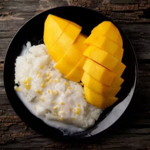 Mango sticky rice with coconut milk and yellow mung beans on a black plate.
