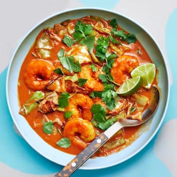 Thai red curry with shrimp, vegetables, cilantro, and lime wedges in a light blue bowl.
