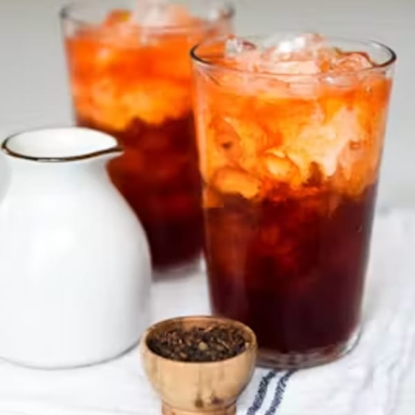 Two glasses of Thai iced tea with a creamer pitcher and a small bowl of tea leaves.